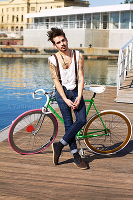 Buy stock photo Bicycle, fashion and young man by the sea in a punk or rock outfit on an urban holiday. Tattoo, confidence and portrait of a serious grunge or edgy gen z male person with a bike by a lake boardwalk
