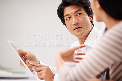 Buy stock photo Shot of two asian business colleagues sitting with a digital tablet and discussing work
