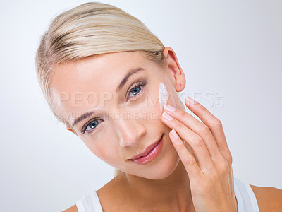 Buy stock photo A beautiful young woman applying moisturiser to her face