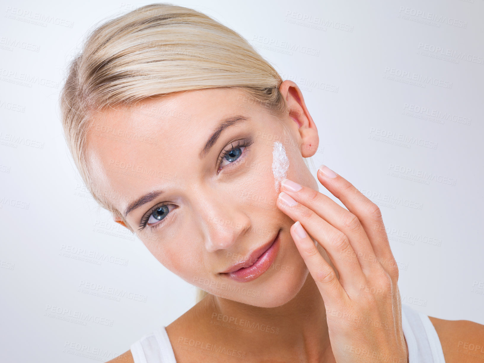 Buy stock photo A beautiful young woman applying moisturiser to her face