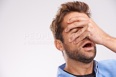 Buy stock photo Studio shot of a handsome young man covering his eyes in regret against a gray background