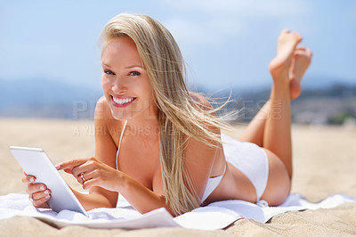 Buy stock photo A tanned woman relaxing on the beach while using her tablet