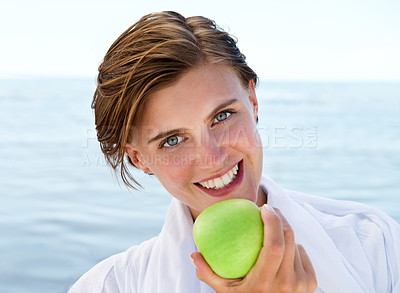 Buy stock photo Ocean, portrait and happy woman eating apple for healthy food, diet and wellness in outdoor morning. Fruit, smile and face of female person for vitamins, fiber and snack in summer at beach