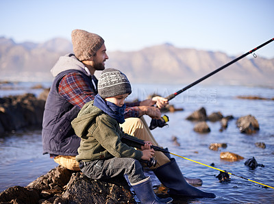 Buy stock photo Father, fishing rod and young boy on rocks, shoreline and bonding for activity by ocean. Sea, catch and learning how to fish for childhood development, winter and hobby while on seaside vacation