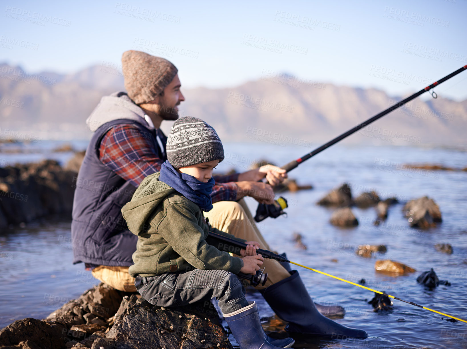Buy stock photo Father, fishing rod and young boy on rocks, shoreline and bonding for activity by ocean. Sea, catch and learning how to fish for childhood development, winter and hobby while on seaside vacation