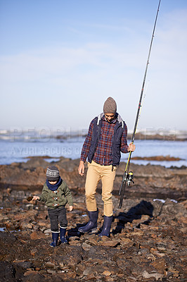 Buy stock photo Shot of a father and son walking on the rocks while out fishing together by the sea