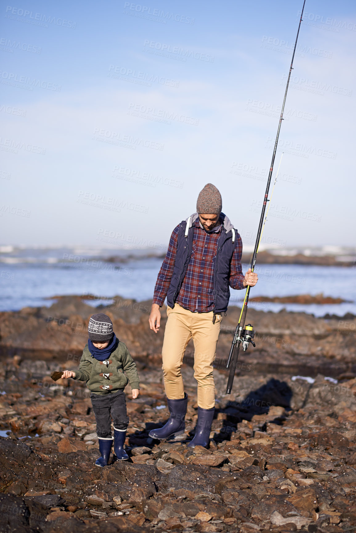 Buy stock photo Shot of a father and son walking on the rocks while out fishing together by the sea
