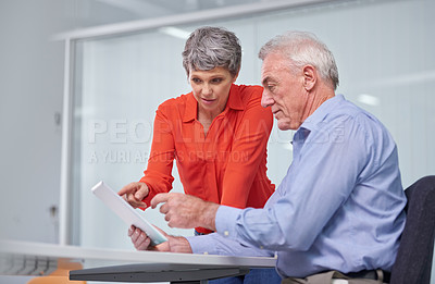 Buy stock photo Shot of two mature business colleagues sitting with a digital tablet and discussing work