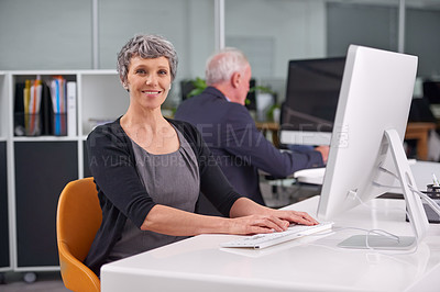 Buy stock photo Portrait of a smiling mature businesswoman at her desk with a coworker in the background
