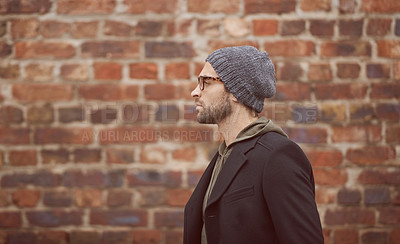 Buy stock photo Shot of a handsome young man in trendy winter attire standing in front of a brick wall