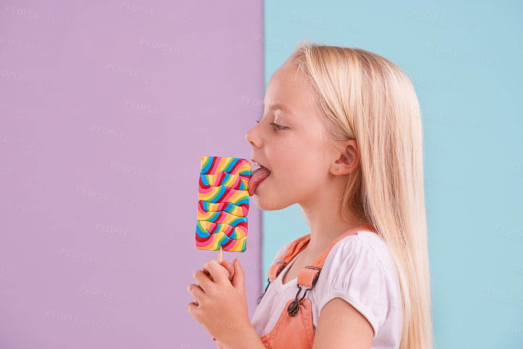 Buy stock photo Studio, girl and lick with lollipop, dessert and choice for snack and childhood. Child, sweets and yummy candy for tasty, eating and happy or excited on vibrant split pastel pink and blue background