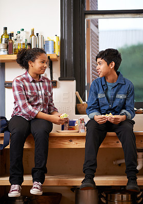 Buy stock photo Shot of two young teenagers enjoying a snack together in the kitchen