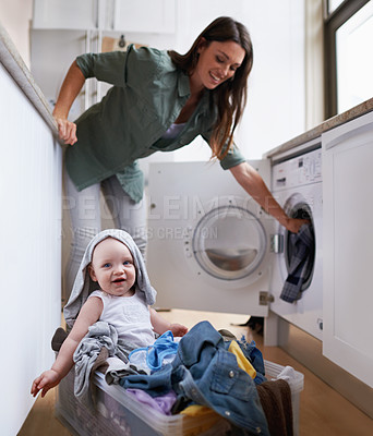 Buy stock photo A mother doing laundry while keeping an eye on her baby