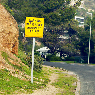 Buy stock photo Signage with warning, road and city with nature, outdoor and board with urban town or funny. Direction, icon or street with symbol, rock or trees with humor or language with bushes, stone or safety