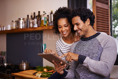Buy stock photo Shot of a young couple using their tablet together while they get ready to prepare a meal