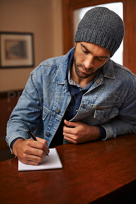 Buy stock photo Shot of a handsome young man sitting at the bar and writing on a piece of paper