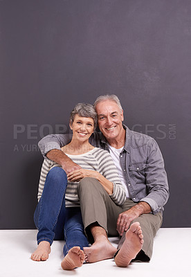 Buy stock photo A happy senior couple sitting together and smiling in the studio