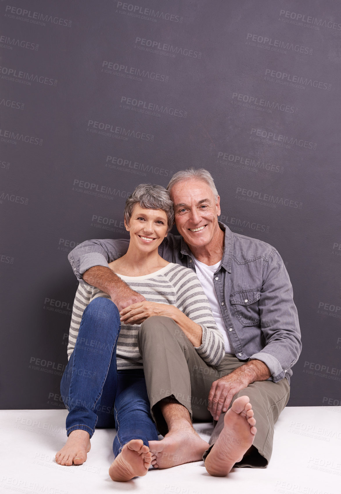 Buy stock photo A happy senior couple sitting together and smiling in the studio