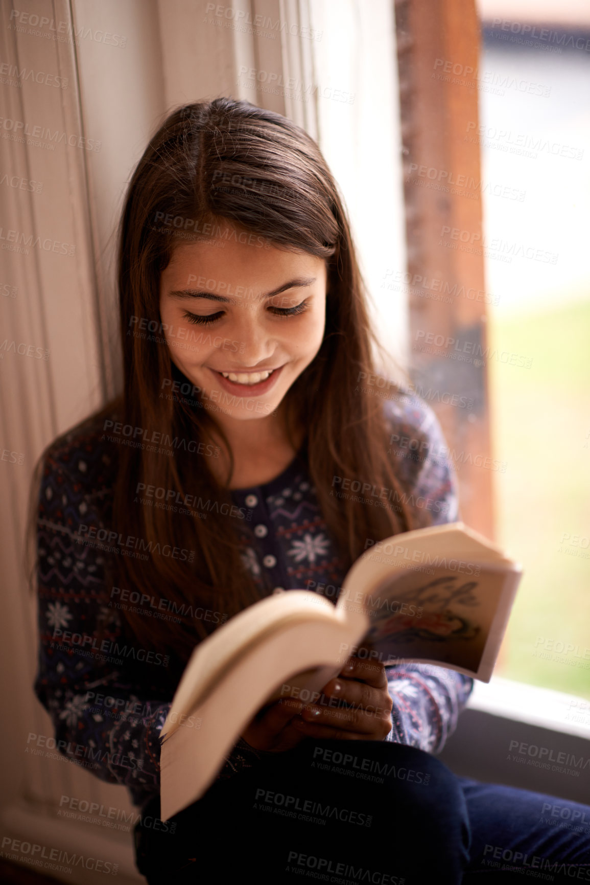 Buy stock photo Girl, kid and book with smile in home for reading, learning and language by window for studying. Child, literacy and thinking with story, happy and fantasy with education in family house in Madrid