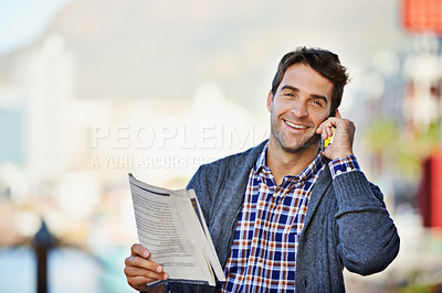 Buy stock photo Shot of a handsome man holding the newspaper and using his phone outdoors