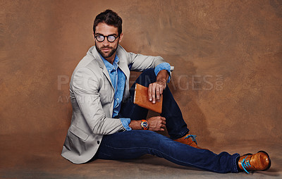 Buy stock photo Fashion, book and man with glasses in studio with trendy, stylish and classy suit on floor. Reading, story and handsome male person with elegant style for outfit and novel by brown background.