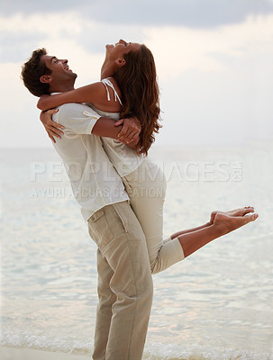 Buy stock photo Young man lifting his gorgeous girlfriend into the air while on the beach