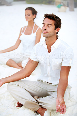 Buy stock photo A young couple meditating in the lotus position on the beach