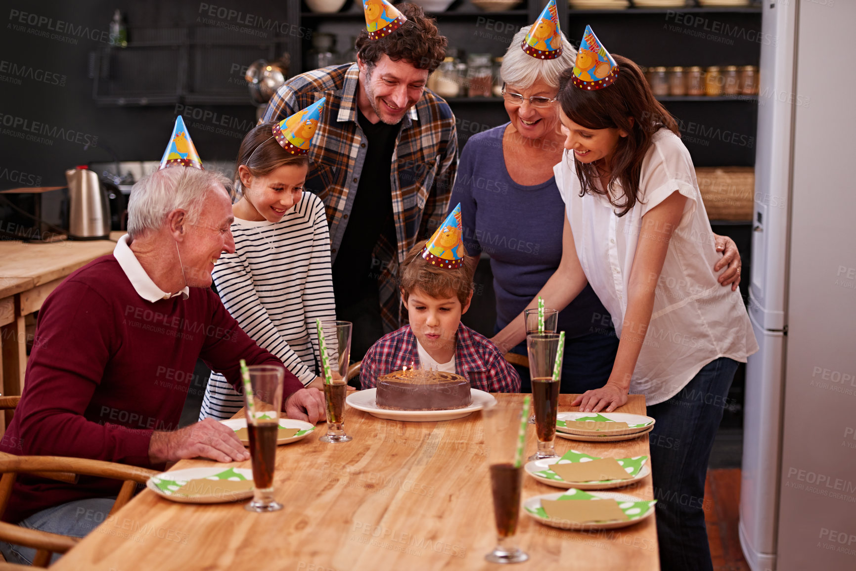 Buy stock photo Family, birthday cake and blowing candle with kid, parents and grandparents together for eating. Happy, smile and dessert with children and celebration with event food and party hats at a table