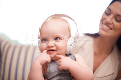 Buy stock photo Shot of an adorable baby girl wearing headphones while sitting with her mother