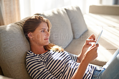 Buy stock photo Shot of a young woman using a digital tablet on her sofa at home