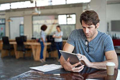 Buy stock photo Shot of a young man working on a digital tablet in an office