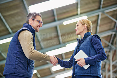 Buy stock photo Shot of two people shaking hands in a large warehouse