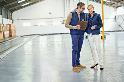 Buy stock photo Shot of two coworkers talking while standing in a large warehouse