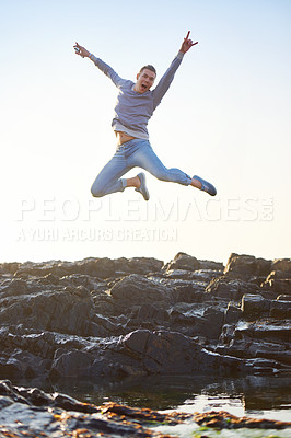 Buy stock photo Shot of a handsome young guy jumping on a rocky beach