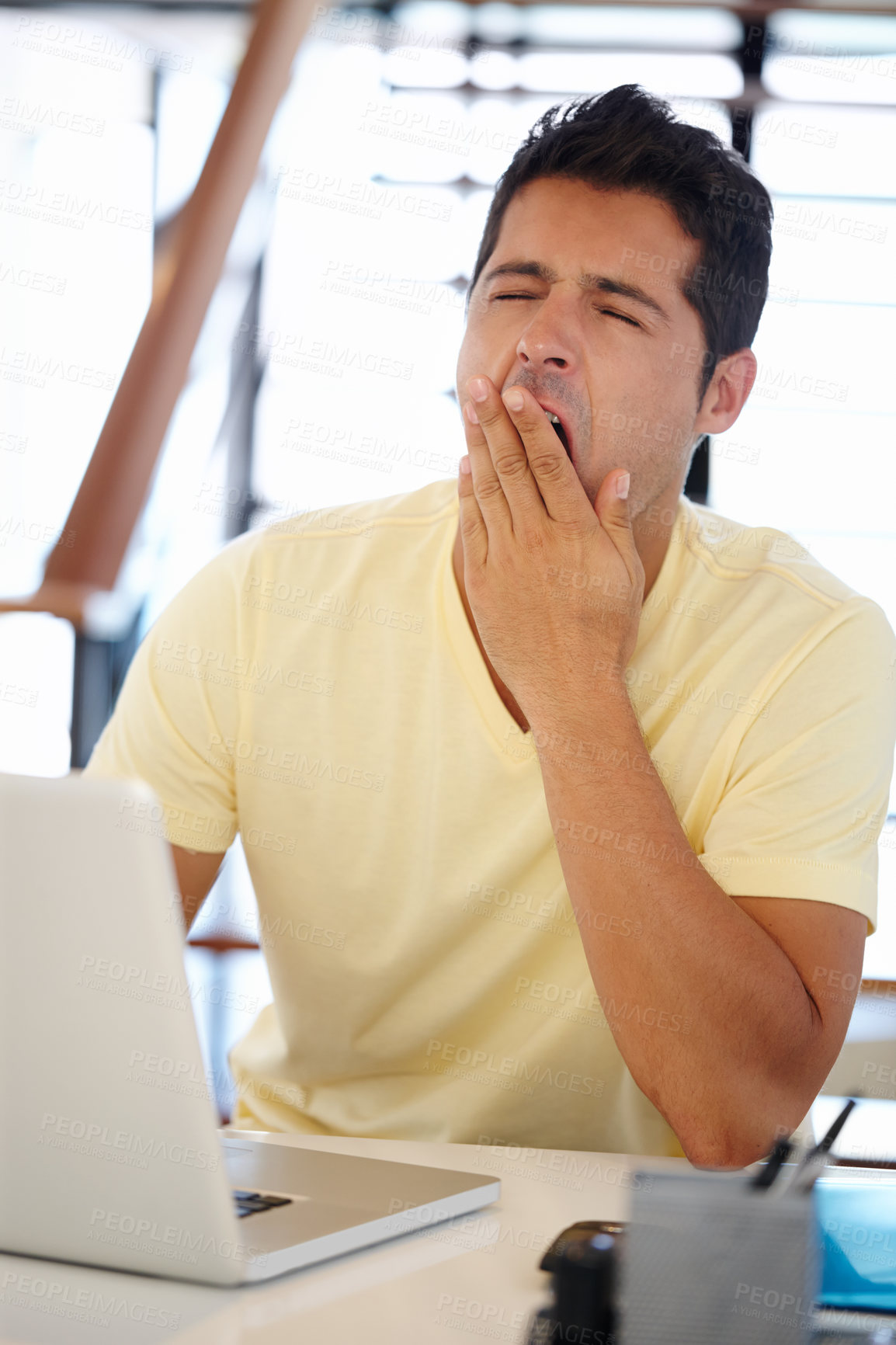 Buy stock photo A young man yawning while sitting at a desk in front of a computer
