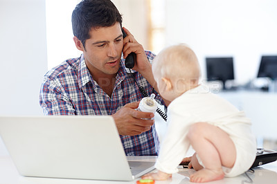 Buy stock photo Shot of a working dad giving his baby a bottle while on the phone