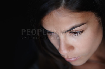 Buy stock photo Closeup of a worried young woman's face and head in a dark room looking thoughtful and contemplating serious decisions. Thinking about problems, anxious about an emotional breakup in dim lit room