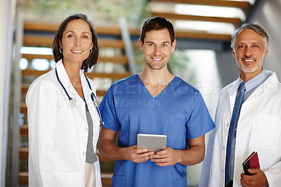 Buy stock photo A cropped portrait of a handsome young doctor standing with a tablet in between two of his colleagues