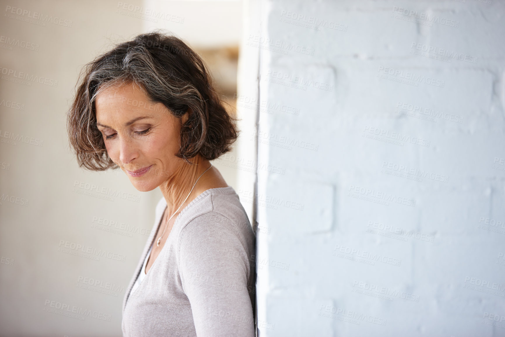 Buy stock photo Shot of an attractive mature woman leaning against a wall