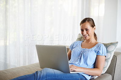 Buy stock photo Shot of an attractive young woman using a laptop in a comfortable position on the sofa