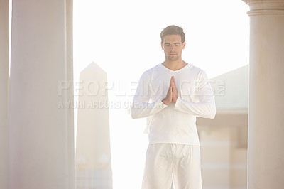 Buy stock photo A man meditating at a spiritual outdoor retreat in the morning. Young religious tourist praying under temple pillars. Young yogi practicing yoga outdoors in a calming and peaceful environment