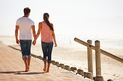 Buy stock photo Rear view shot of a young couple walking along the beach holding hands