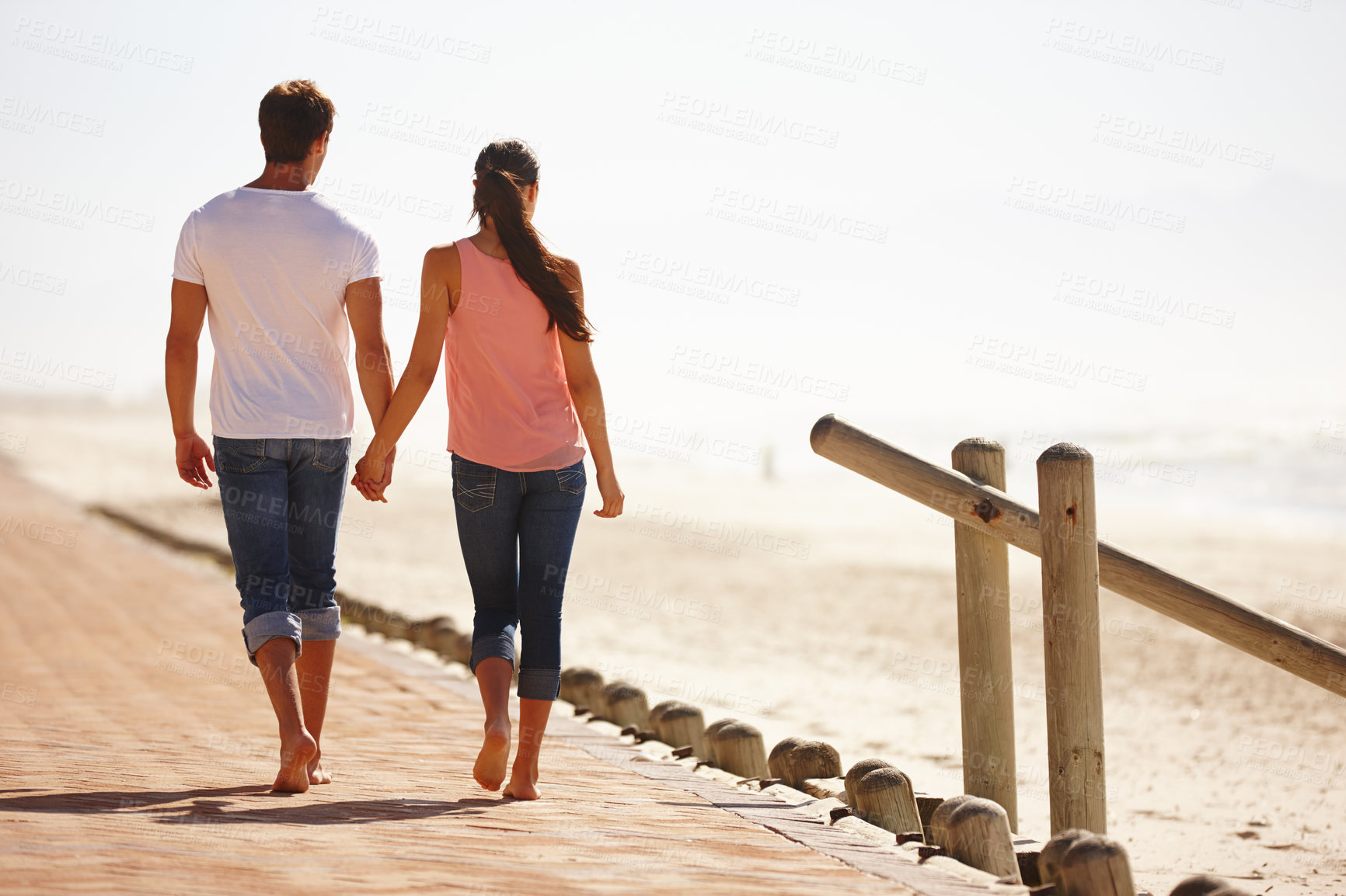 Buy stock photo Rear view shot of a young couple walking along the beach holding hands