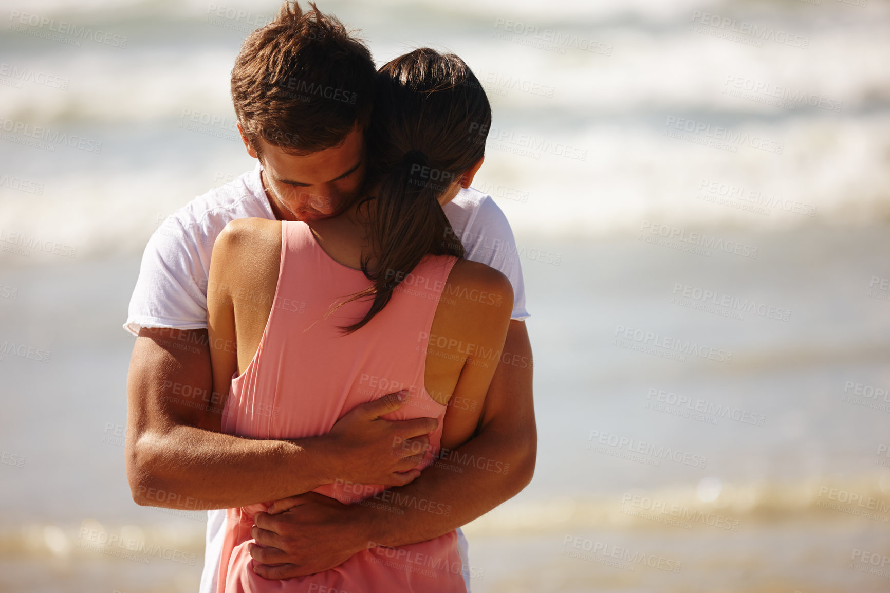 Buy stock photo Cropped shot of a young man comforting his girlfriend while standing on the beach