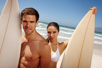 Buy stock photo Shot of a young couple holding surfboards at the beach