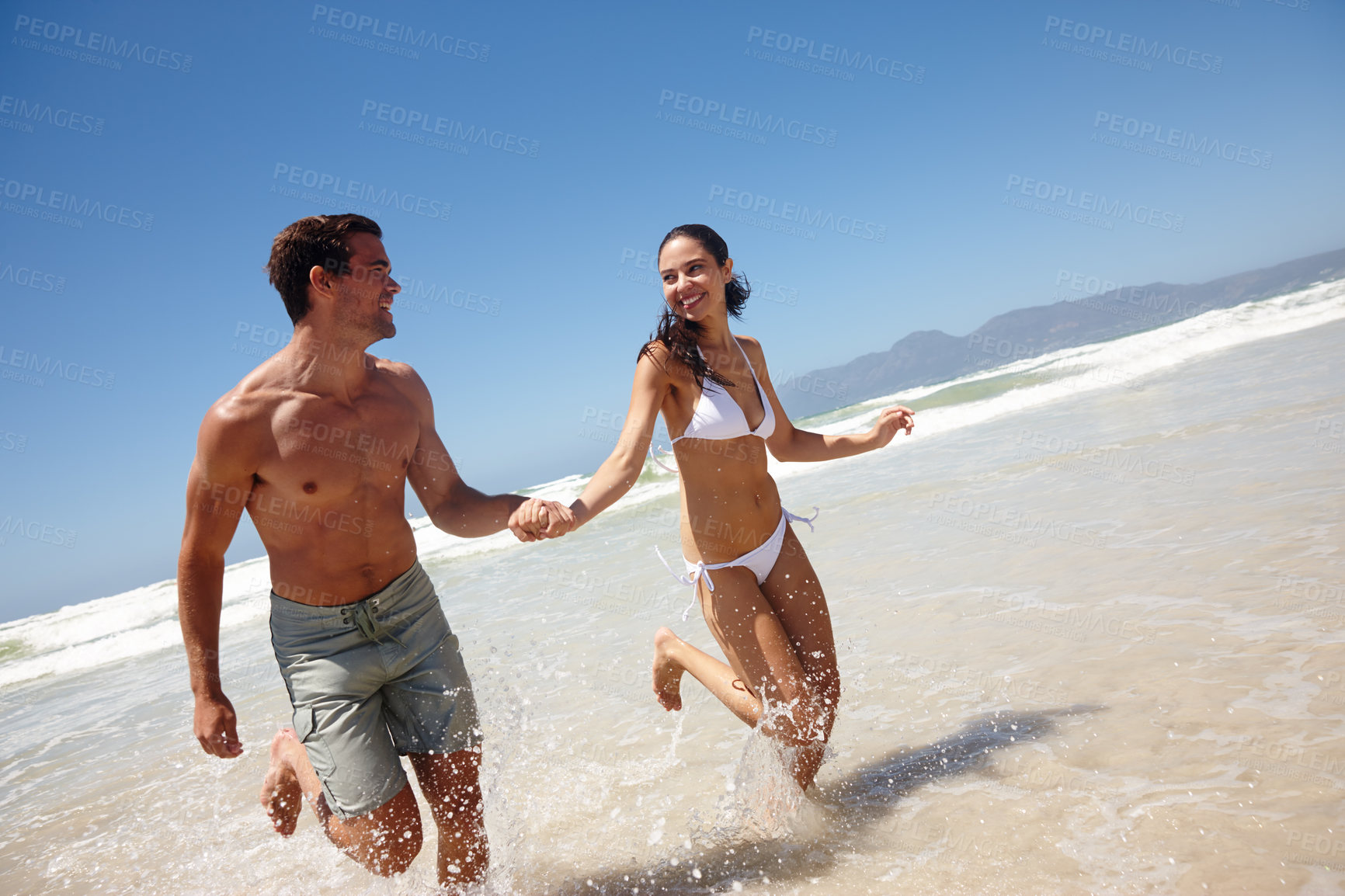 Buy stock photo Shot of a happy young couple running through the water