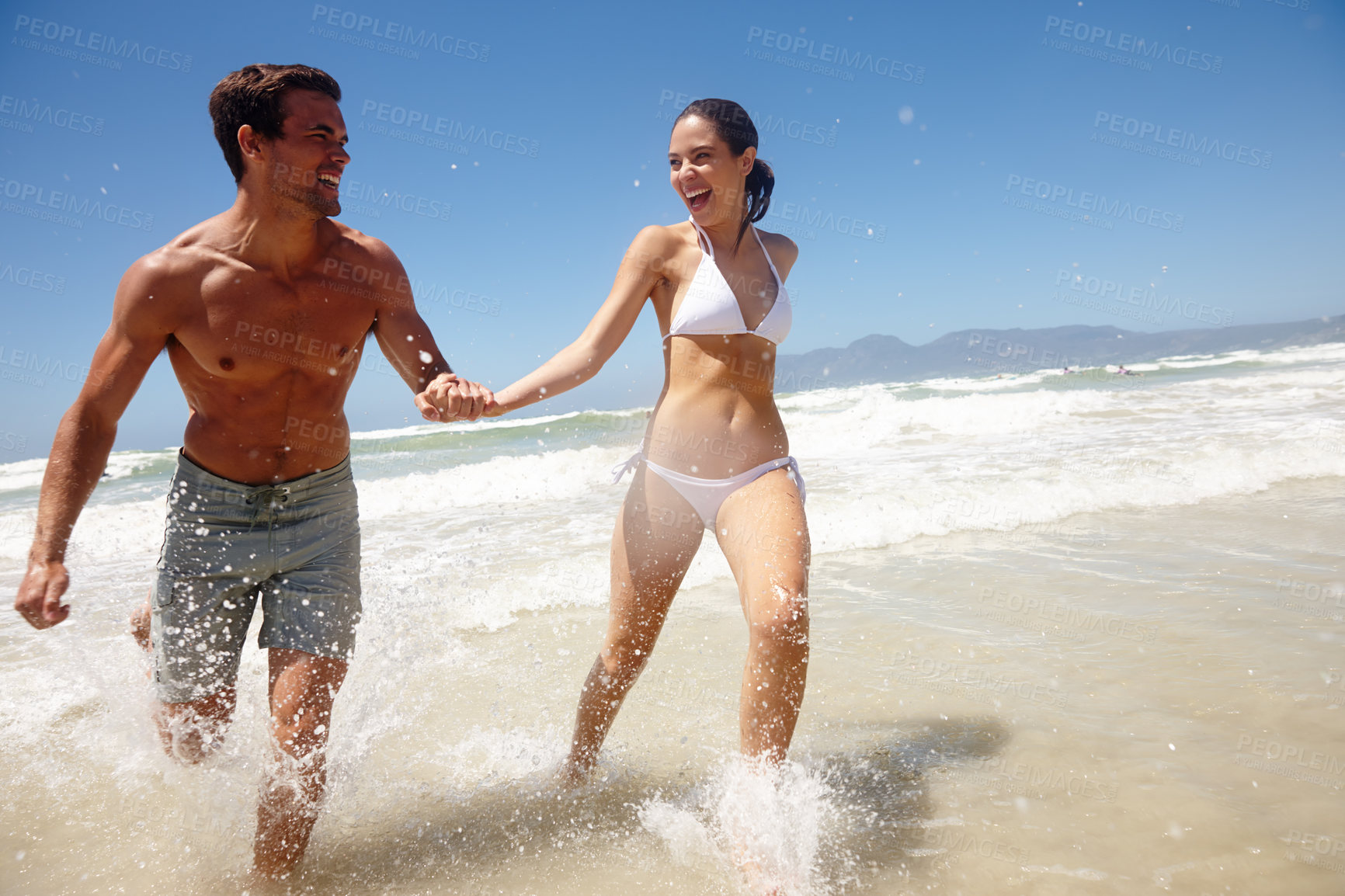 Buy stock photo Shot of a playful couple running through the water at the beach