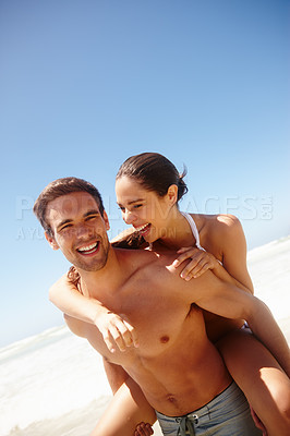 Buy stock photo Cropped shot of a young man piggybacking his girlfriend at the beach