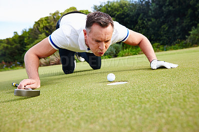 Buy stock photo Shot of a handsome man trying to blow his golf ball into the hole
