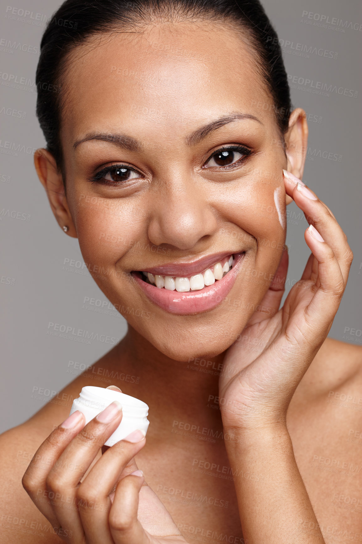 Buy stock photo Cropped shot of a beautiful young woman applying face cream while standing in a studio